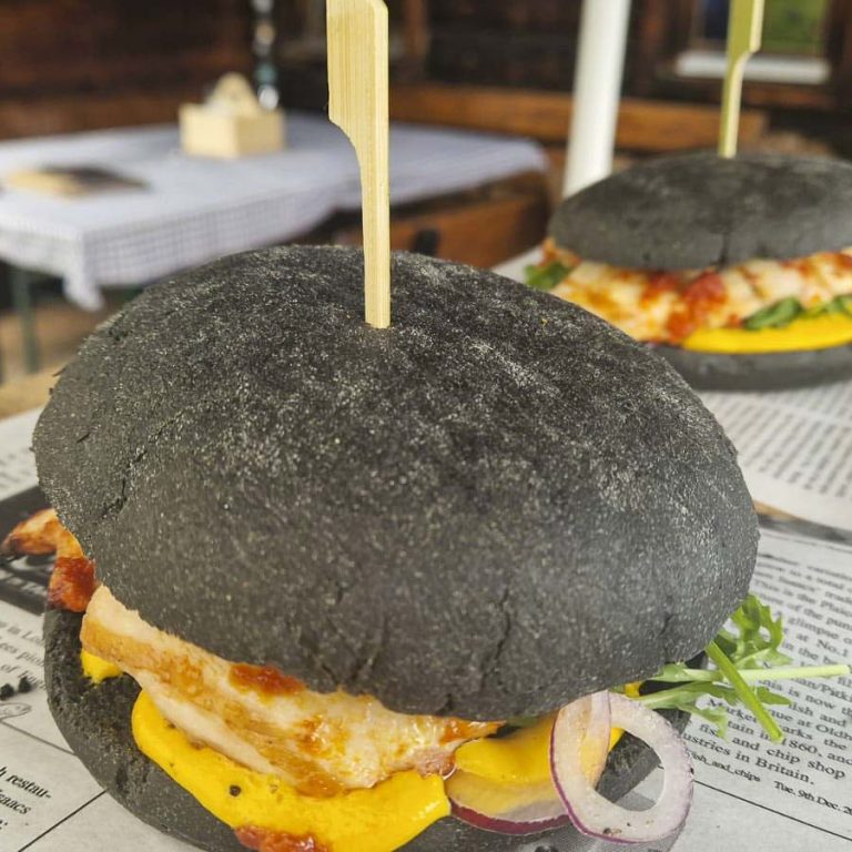 Schwarzer Burger mit Hähnchen, Käse, Zwiebeln und frischem Gemüse.