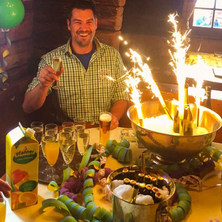 Mann feiert mit Getränken, Funkeln von Feuerwerk und festlicher Dekoration.